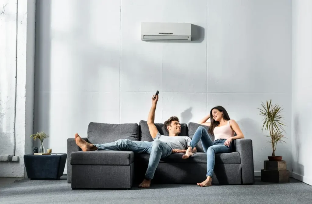 Handsome boyfriend switching on the air conditioner and looking at his smiling girlfriend.