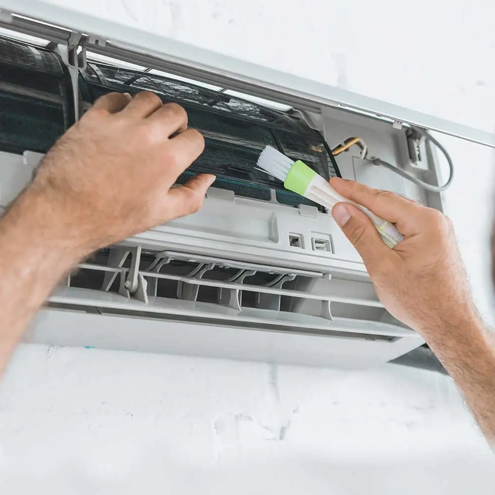 A person in a white shirt works on a white wall-mounted electrical panel, removing a green outlet with a white electric tool.